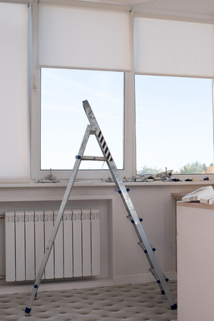 Stepladder stairs in the apartment by the window against the background of repair materials. Vertical photoの写真素材