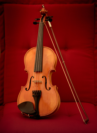 Violin and bow on a red fabric pillow. Close up of violin and bow on red pad in general full viewの写真素材