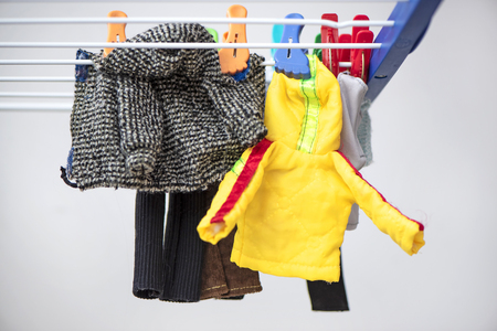 Doll clothes hanging on clothespins on the dryer. Drying baby clothes, close up. Different clothes hanging with colorful pins on the clotheshorse for dryingの写真素材