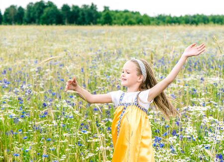 Little pretty girl in yellow Russian dress is dancing on field of wild flowers on summer day. Cute child smiling girl in chamomile field. concept of Russian traditions and folklore.の写真素材