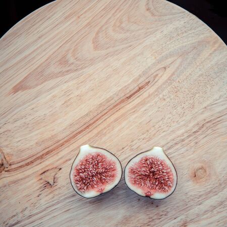 A two cross section figs. One fig sliced in half on on wooden board background. Focus is on the sliced fig. Top view, copy space.の写真素材
