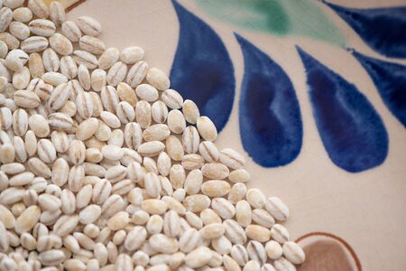 Dry pearl barley grain seed close up on colorful bowl plate on table, top viewの写真素材