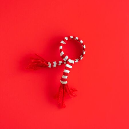 Christmas minimalistic composition. White and red striped scarf decoration on red paper background....