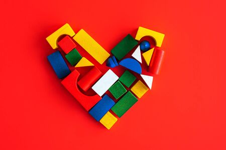Wooden bright geometric shapes on colorful heart on red, multi colored education toy for kid on red paper backgroundの写真素材