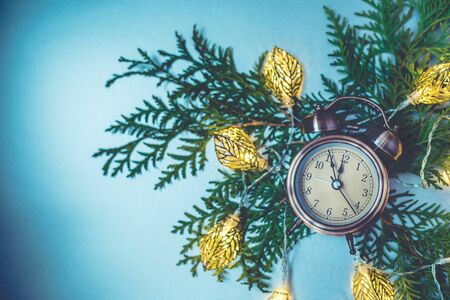 Close up of retro alarm clock on Christmas background with green branch and garland. Retro toned,...