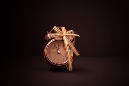 Close up of retro alarm clock in golden bow on bown background. Copy space.の写真素材