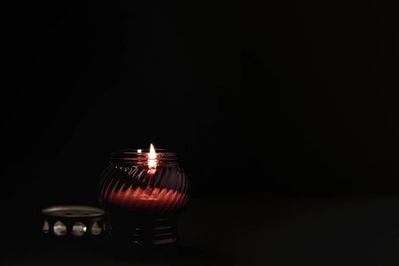 White burning candle in red glass on black background. Mourning, burning candle. Mourning, sadness,...