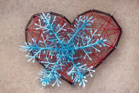 Big Tinsel Snowflake on close-up of red heart made of threads, stranded between the nails. The...
