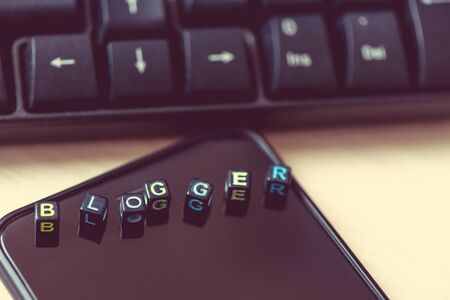 Close up words BLOGGER on blocks on black smart phone on desk near the keyboard and mouse of the computerの写真素材