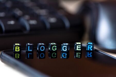 Close up words BLOGGER on blocks on black smart phone on desk near the keyboard and mouse of the...