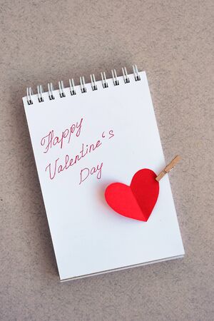 Notebook with handwritten text: happy valentines day and a heart cut out of red paper. Top view with copy spaceの写真素材