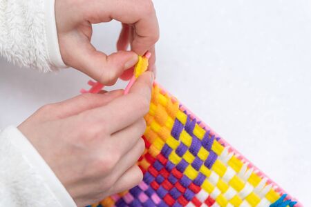 childrens creativity weaving with colored threads ropes on white table. Child hands in work