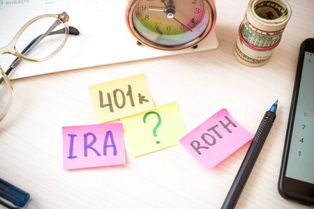 Words 401k ira roth on pieces of colorful paper, money dollars and glasses on table. Pension...