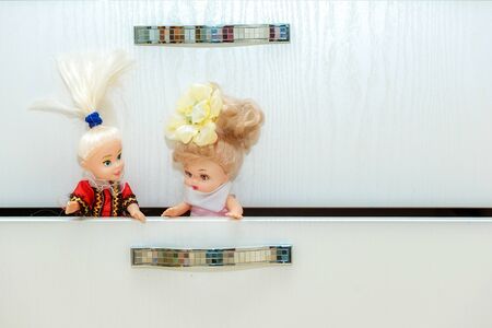 Two pretty dolls sitting in a cabinet drawer in nursery, playroom. Lot of toys in children's roomの写真素材
