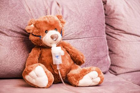 Child makes the procedure to his toy, Teddy Bear with an inhaler nebulizer. Inhalation at home for cough health and allergy, Health concept. Playing at the hospital at home, no people.の写真素材