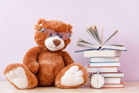 Soft stuffed toy Teddy bear with glasses, a stack of books and a stopwatch. Education concept, back to school, reading speedの写真素材