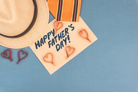 Happy Father's Day inscription with tie, hat handmade hearts on blue background. Greetings and presentsの写真素材