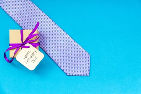 Happy Fathers Day inscription with tie and gift craft box on blue background. Greetings and presentsの写真素材