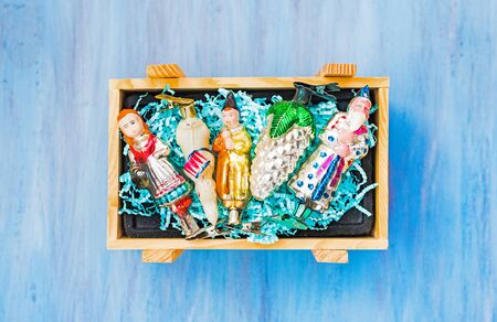 Old christmas glass toy baubles in wooden packaging box with paper straw for fragile objects on blue...