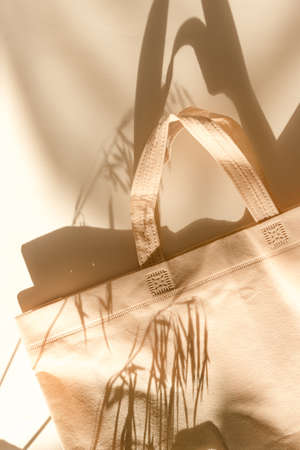 Beige eco bag, shopping sack lies on the white table on morning sunlight. Shadows from bag and plants.の写真素材