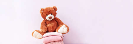 Brown stuffed teddy bear sitting on stack of clean cotton towels or clothes. Childhood care,...