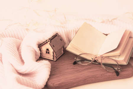 Reading books on pastime, calm weekends or vacations at home. Soft woolen plaid, sweater or blanket. Old-fashioned glasses and wooden house miniature model. Cosiness and comfort in apartmentの写真素材