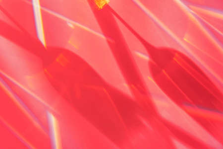 Sunshine reflection and shadows through wineglasses. Sun glare texture on red blurry background....