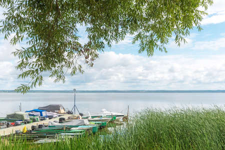 Long pier with moored boats on river with reeds on bankの写真素材