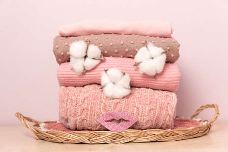 Stack of folded wool knitted sweaters or pullovers in pink pastel colors on table with made fece of cotton flower. Close up of warm cozy comfortable monochrome clothes for autumn winter season.の写真素材