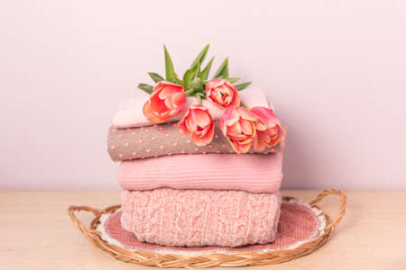 A stack of womens knitted sweaters on a wicker tray on a shelf, next to a bouquet of flowersの写真素材