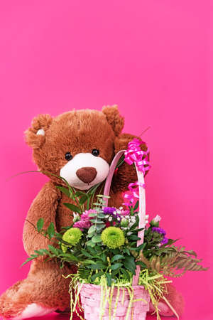 Teddy bear holding blank card and small bouquet on pinkの写真素材