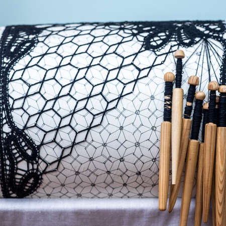 Elegant black unfinished lace and set of wooden bones on white paper cylinder with drawing in light room extreme close viewの写真素材