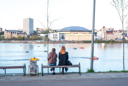 Women sit on bench looking at river with boats in eveningのeditorial素材