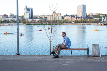 Mature man with glasses rests on bench against calm riverのeditorial素材