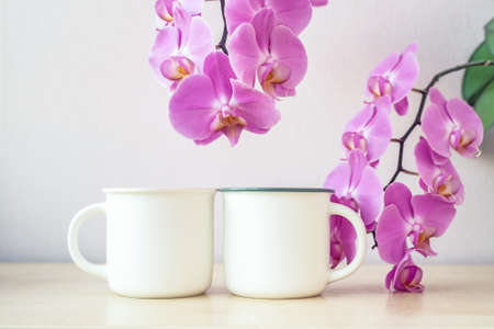 Mockup of two white mugs on table with orchid flowers decorの写真素材