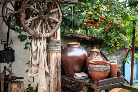 Clay pots on rack by beam with hanging wagon wheels in yardの写真素材