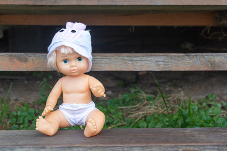 Cute kewpie doll sits on wooden bench in country house yardの写真素材