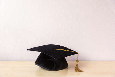 Academic cap with tassel on wooden table near pastel wall