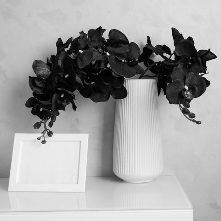 Orchid flowers in vase and photoframe on cabinet by wall