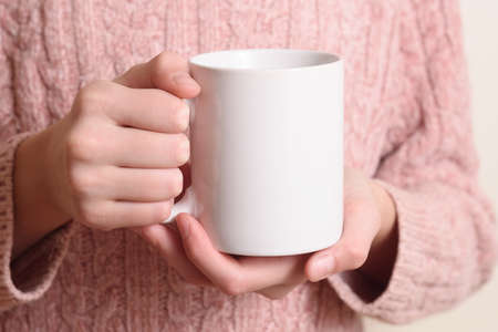 Young woman in warm sweater is holding white mug in hands