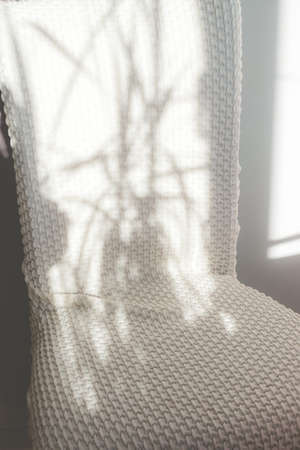 Chair in white fabric cover on the veranda, in sunlight and plant shadows