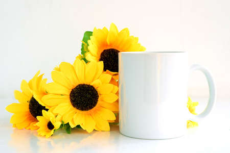 White coffee mug blank mockup with bouquet of yellow sunflowers, copyspace.