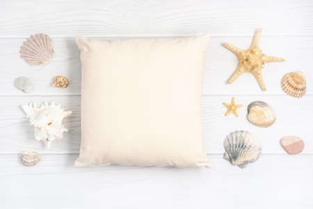 Flat lay mockup of beige square cushion with shell, seashell, starfiish on a white wooden...