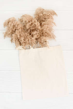 Fall vertical mockup with tote bag blank and dry reeds on white wood background. Boho totebag mock up grass for decoration design. Shopping bag, handbag. Ecology concept.の写真素材