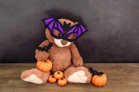 Funny brown teddy bear with bat mask and pumpkins on old wooden table by dark wallの写真素材