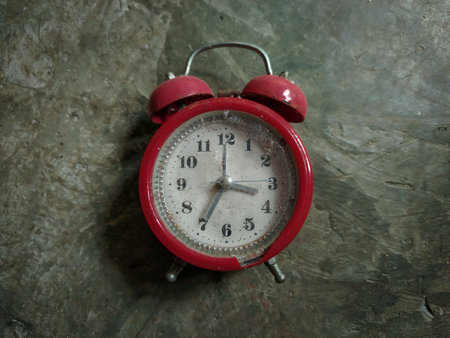 Old-fashioned red alarm clock placed on cement floor, isolated object for lifestyle and time concept.の写真素材