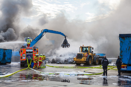 Firefighters attending to a blaze with a fire engine using a fire hose and extended ladder to spray water on the smoke and flamesの写真素材