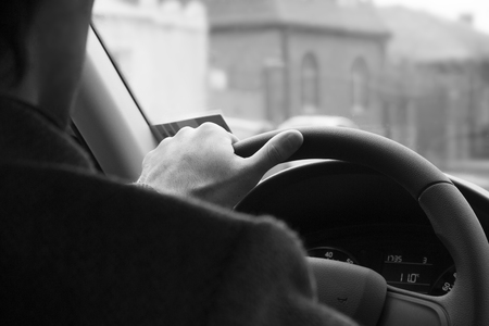 Male driver hands holding steering wheel.Driving safety in the city. background black and whiteの写真素材