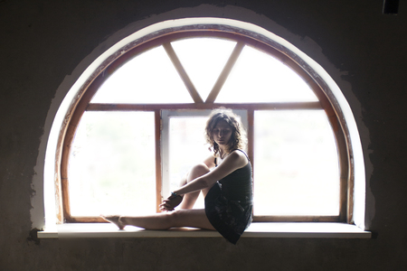 Portrait of a beautiful young bride sitting on a window semicircular sill round window.の写真素材