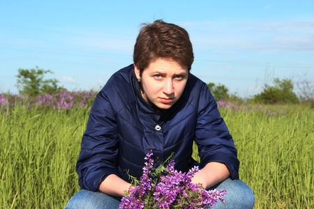 Beautiful girl sitting with her legs crossed. In the hands of a bouquet. The girl looks skeptical and serious. It does not look feminineの写真素材